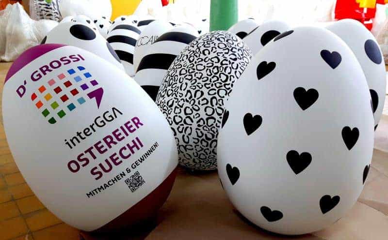 Ostereier 2 Kolorowe, ozdobne jajka wielkanocne, w tym jedno z napisem "D' GROSSI interGGA OSTEREIER SUECHI MITMACHEN & GEWINNEN".