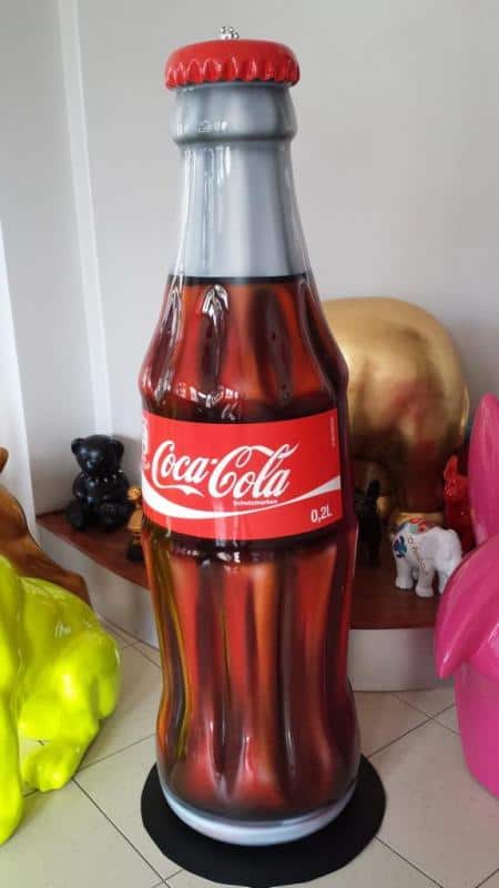 Hängende Coca-Cola-Flaschen. 4 Duża dekoracyjna butelka Coca-Coli o objętości 0,2 litra, stojąca w pomieszczeniu wśród różnych kolorowych figurek.