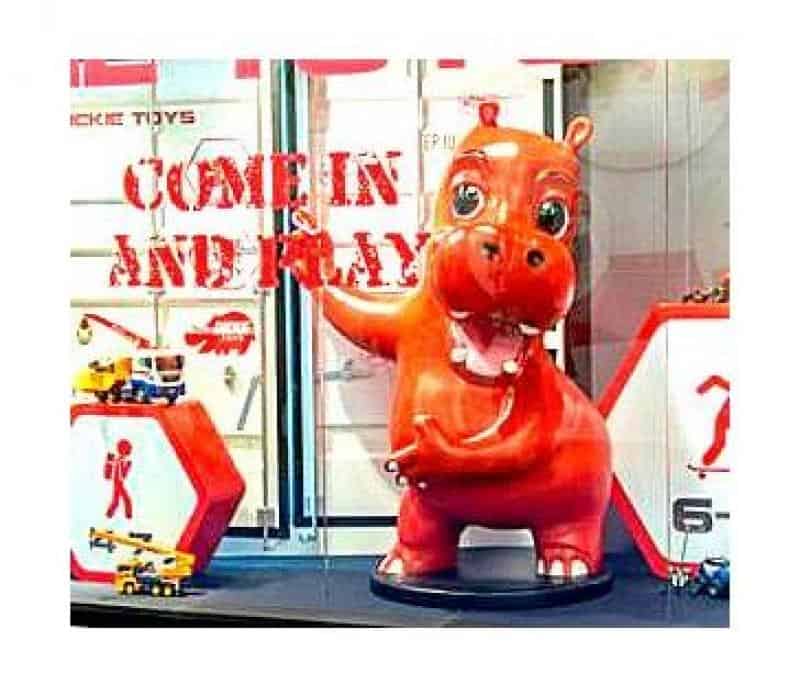 Werbe-Hippo 2 Czerwona figurka hipopotama w witrynie sklepowej z napisem "COME IN AND PLAY".