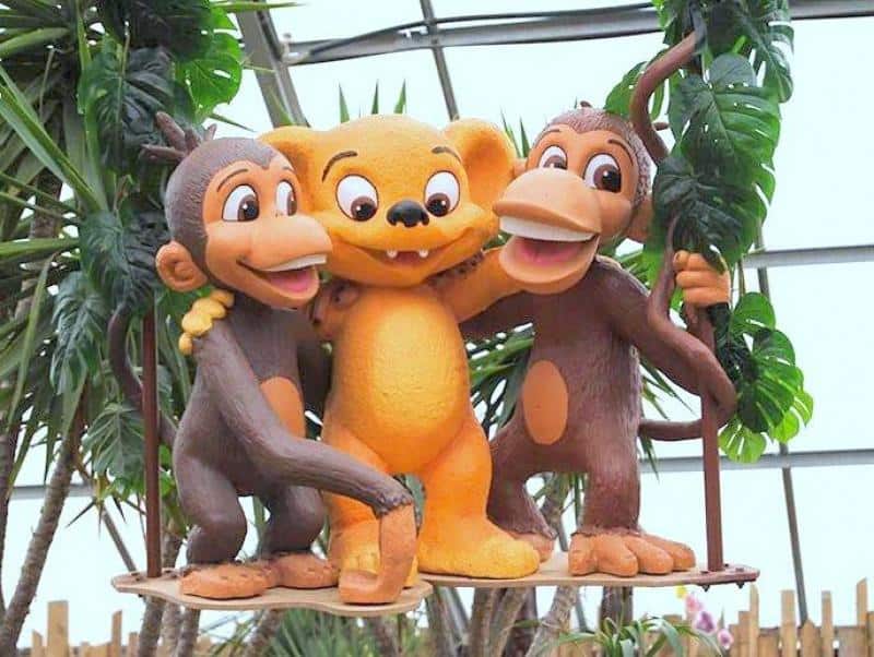 Figuren für Freizeitpark - Hugo Land 2 Trzy postacie kreskówkowe: dwa małpy i jeden stwór o pomarańczowej sierści, stoją razem na huśtawce w otoczeniu roślin.