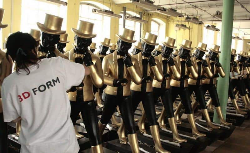 Große Johnnie Walker Figuren 4 Rzędy manekinów ubrane we złote garnitury i cylindry, osoba w białej koszulce z napisem "3D FORM" pracuje przy jednym z nich.