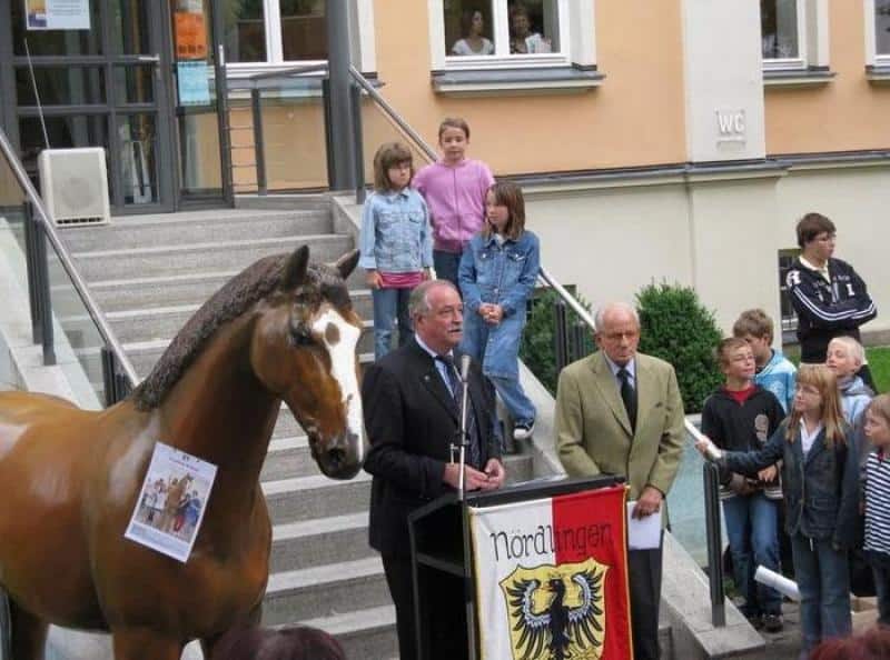 Event-Pferdefiguren 2 Grupa osób podczas ceremonii na zewnątrz, przy posągu konia i mównicy z herbem "Nördlingen".