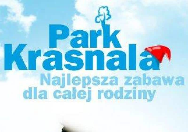 Figuren in einem Themenpark 1 Logo Park Krasnala z napisem "Najlepsza zabawa dla całej rodziny" na tle błękitnego nieba z chmurami.