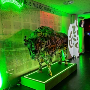 Bison-Skulptur mit Aufschriften, beleuchtet mit grünem Licht, auf einem beleuchteten Sockel in einem Raum.
