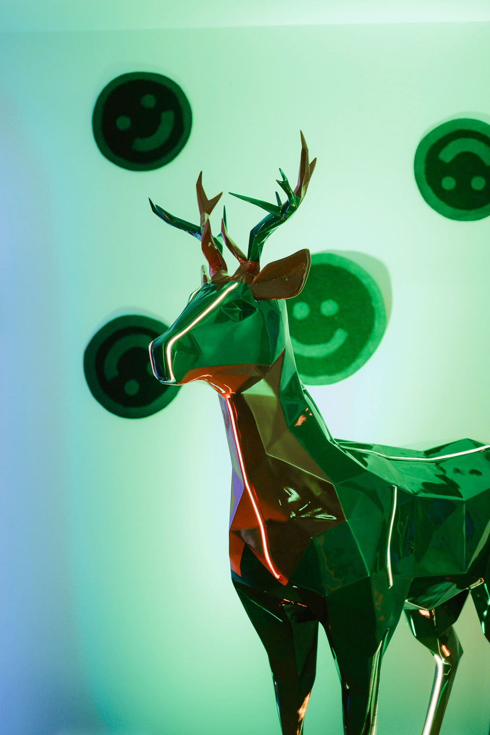 Jägermeister-Hirsche mit LED-Beleuchtung 7 Metaliczna rzeźba renifera na tle świecących, zielonych emoji.
