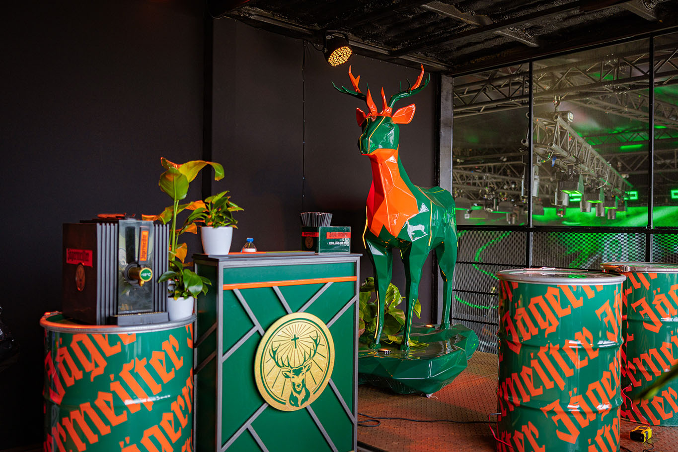 Jägermeister-Hirsche mit LED-Beleuchtung 1 Kolorowy, geometryczny jeleń oraz elementy dekoracyjne marki Jägermeister w barze ozdobionym roślinami.