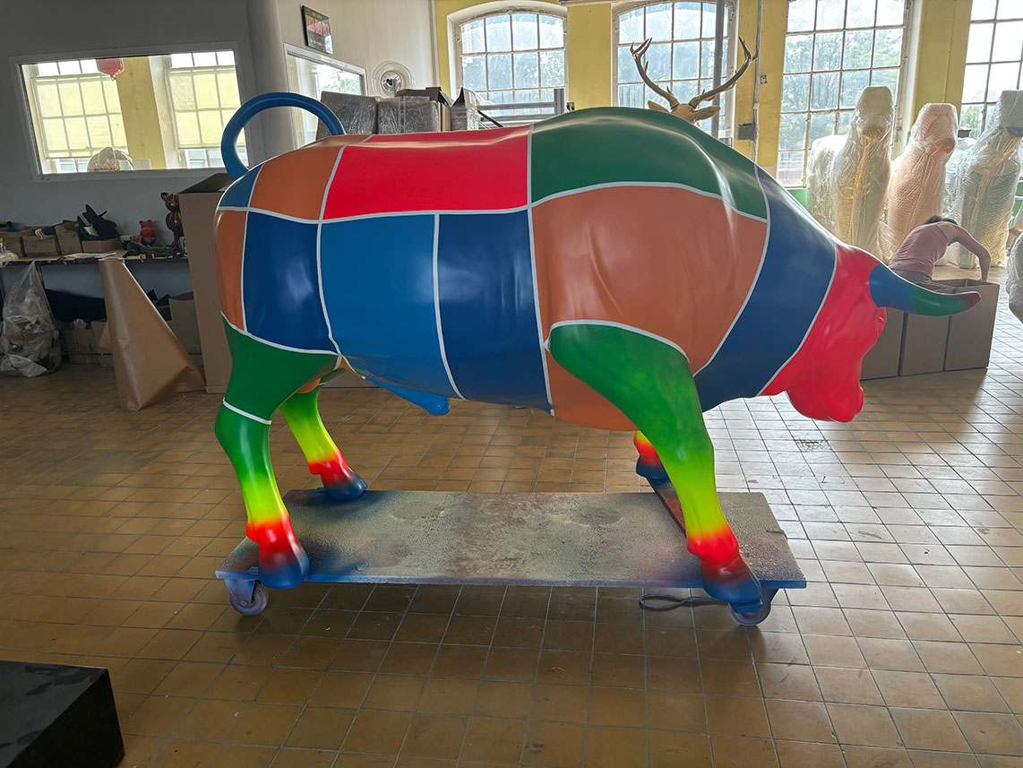 Kolorowa figura z laminatu w kształcie byka pokryta geometrycznymi polami w intensywnych barwach, ustawiona na wózku.