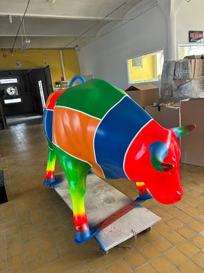 Kolorowa figura z laminatu w kształcie byka, pomalowana w duże wielobarwne pola i gradienty.
